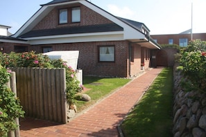 A two-story brick house with a sloped roof, a paved pathway, and a stone wall on one side. - 2 in the Annelene house (Westerland)
