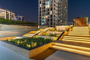 A modern building with multiple floors, a staircase with illuminated steps, and a landscaped area with plants. - Bright 1BR in Dubai Marina with Balcony, Pool and Gym (Dubai)