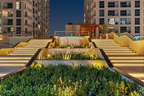 A multi-level outdoor staircase with illuminated steps and a central water feature, surrounded by lush greenery. - Bright 1BR in Dubai Marina with Balcony, Pool and Gym (Dubai)