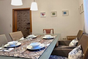 A dining area with a long table set for four, surrounded by wicker chairs. - Holiday apartment with 1 bedroom (Lindau (Bodensee))
