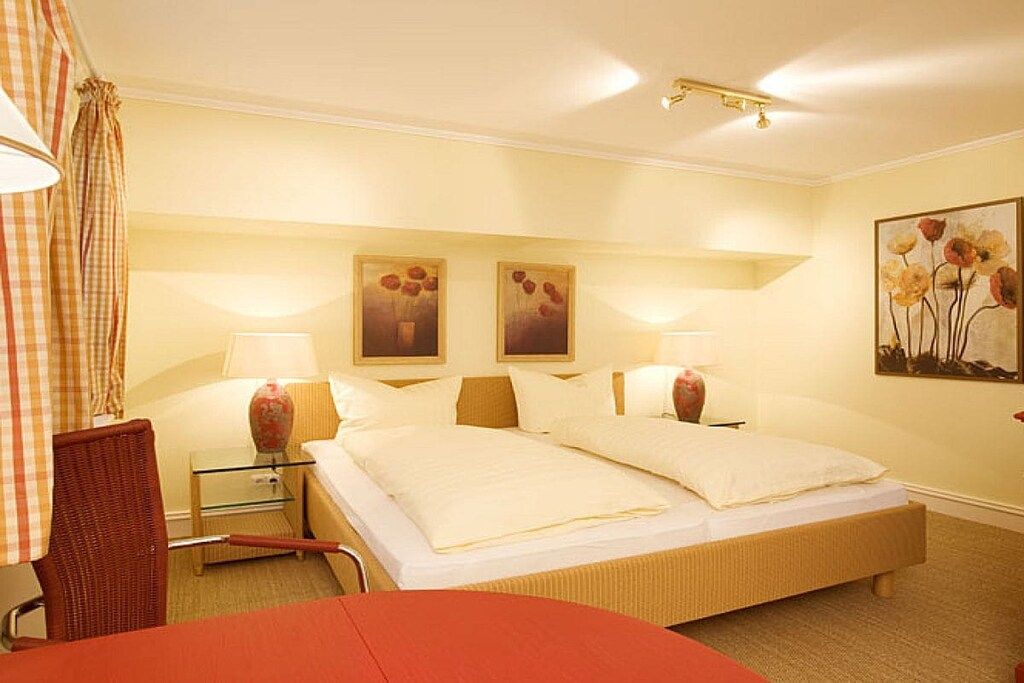 A hotel room with a double bed, two bedside tables with lamps, a chair, and a painting on the wall.