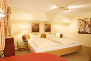 Quarto de hotel com uma cama de casal, duas mesas de cabeceira com abajures, uma cadeira e um quadro na parede.