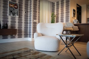 Un moderno salón con un sillón blanco grande, una mesita de centro pequeña y un diseño de papel tapiz a rayas.