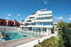 Ein modernes, mehrstöckiges Gebäude mit Glasfassade, Dachterrasse und Schwimmbecken.