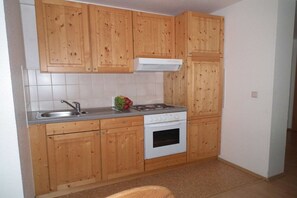 A compact kitchen with wooden cabinets, a stainless steel sink, a gas stove, and a white oven. - in the holiday home Nexö - 2 bedrooms (Ilsenburg)
