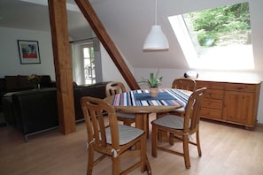 A dining area with a round table, wooden chairs, a potted plant, and a view of greenery through a window. - in the holiday home Nexö - 2 bedrooms (Ilsenburg)
