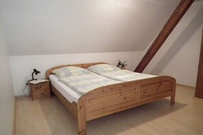 En säng för en person med en träram, ett sängbord med en lampa och en liten växt på golvet.