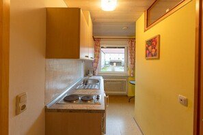 Eine schmale Küche mit Einbauherd, Spüle und einem Fenster mit Vorhängen.