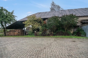 A building with a metal roof, a brick driveway, and a stack of firewood.