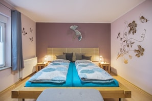 A double bed with a blue and white patterned bedspread, two bedside lamps, a wooden headboard, and decorative wall stickers.