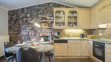Una cuina moderna amb detalls de paret de pedra, armaris de fusta i zona de menjador amb taula per a dues persones.