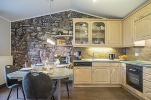 Une cuisine moderne agrémentée de murs en pierre, de meubles en bois et d’un coin repas avec une table mise pour deux personnes.