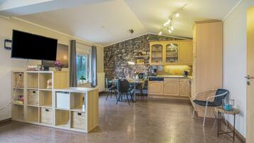 A modern kitchen with stone wall accents, a dining area with chairs, and a flat-screen TV mounted on the wall.