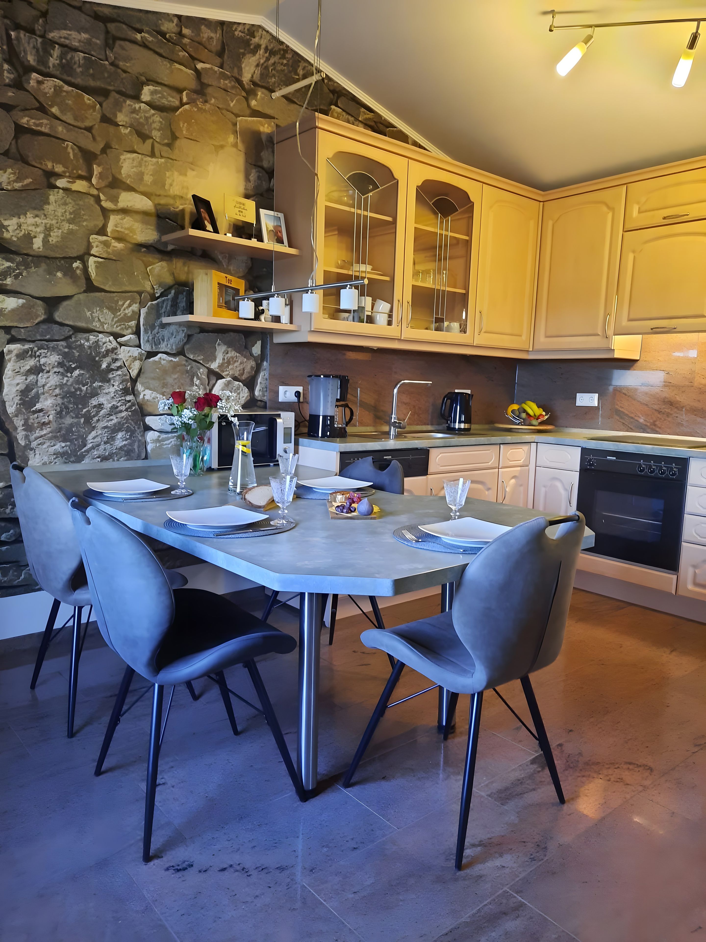 Una cocina moderna con pared de piedra, armarios de madera y una mesa de comedor para cuatro.