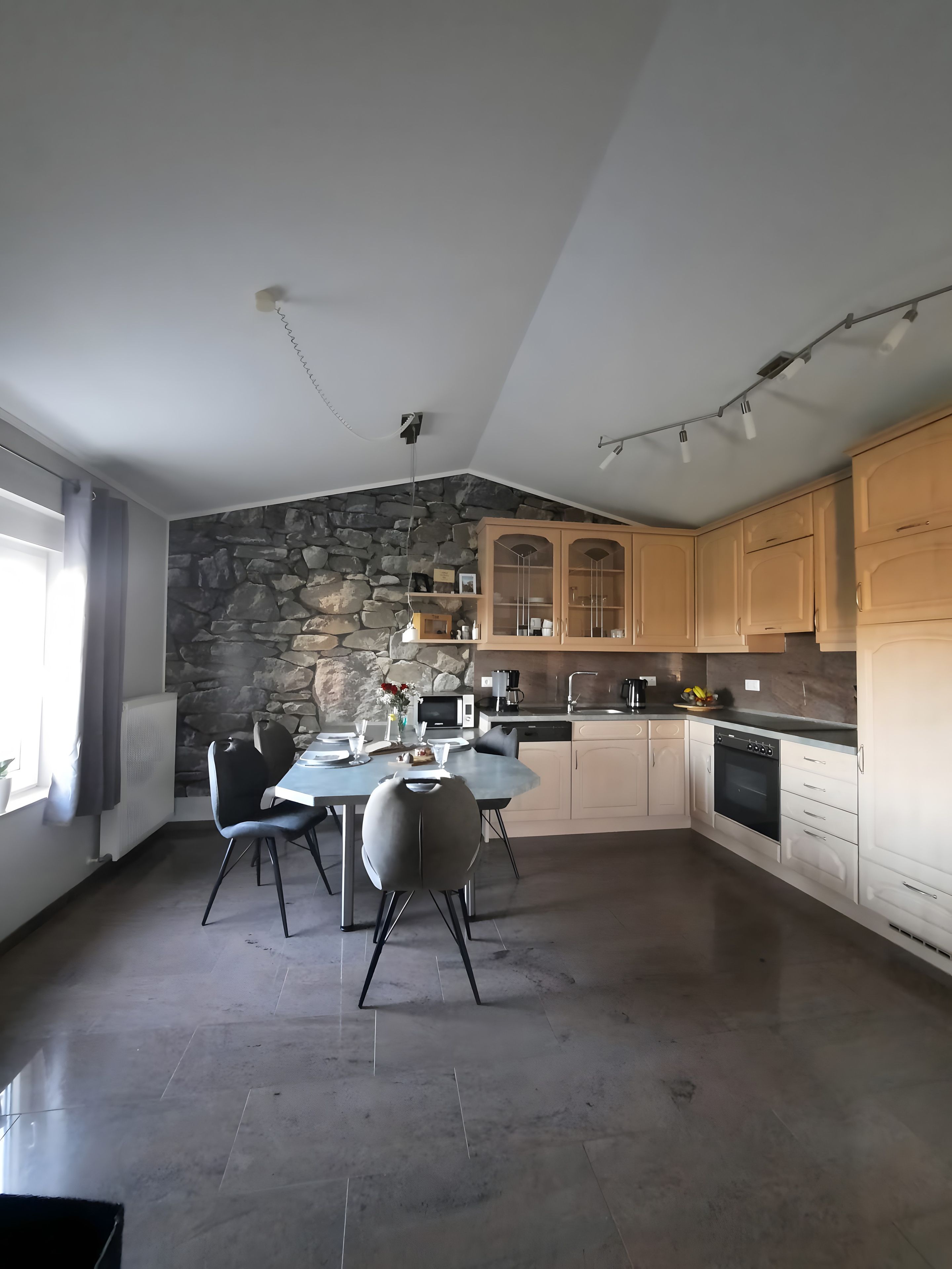 Una cocina moderna con una pared de acento de piedra, armarios de madera y una zona de comedor con sillas.