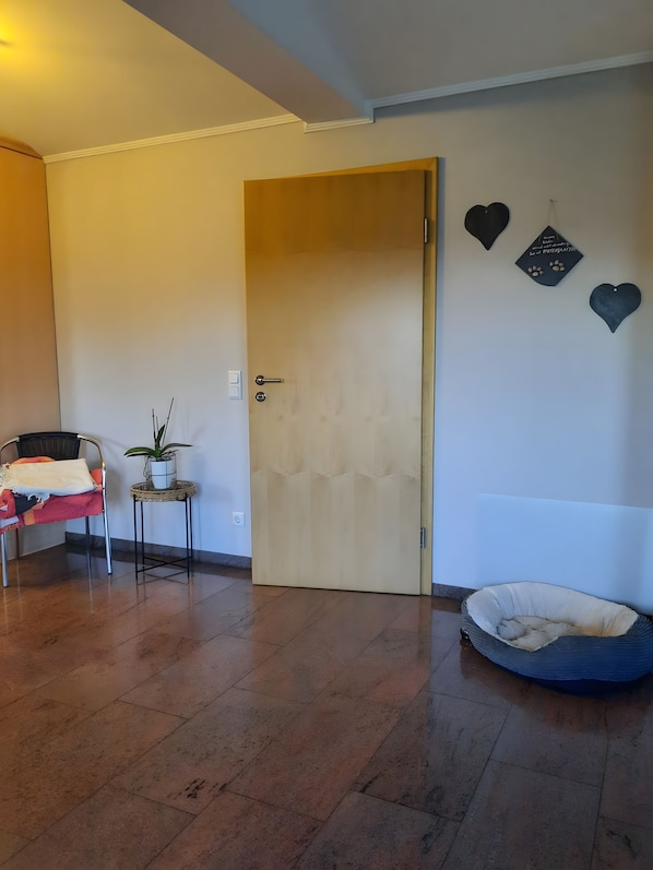 A room with a wooden door, a pet bed, a chair with a blanket, and a small table with a plant.