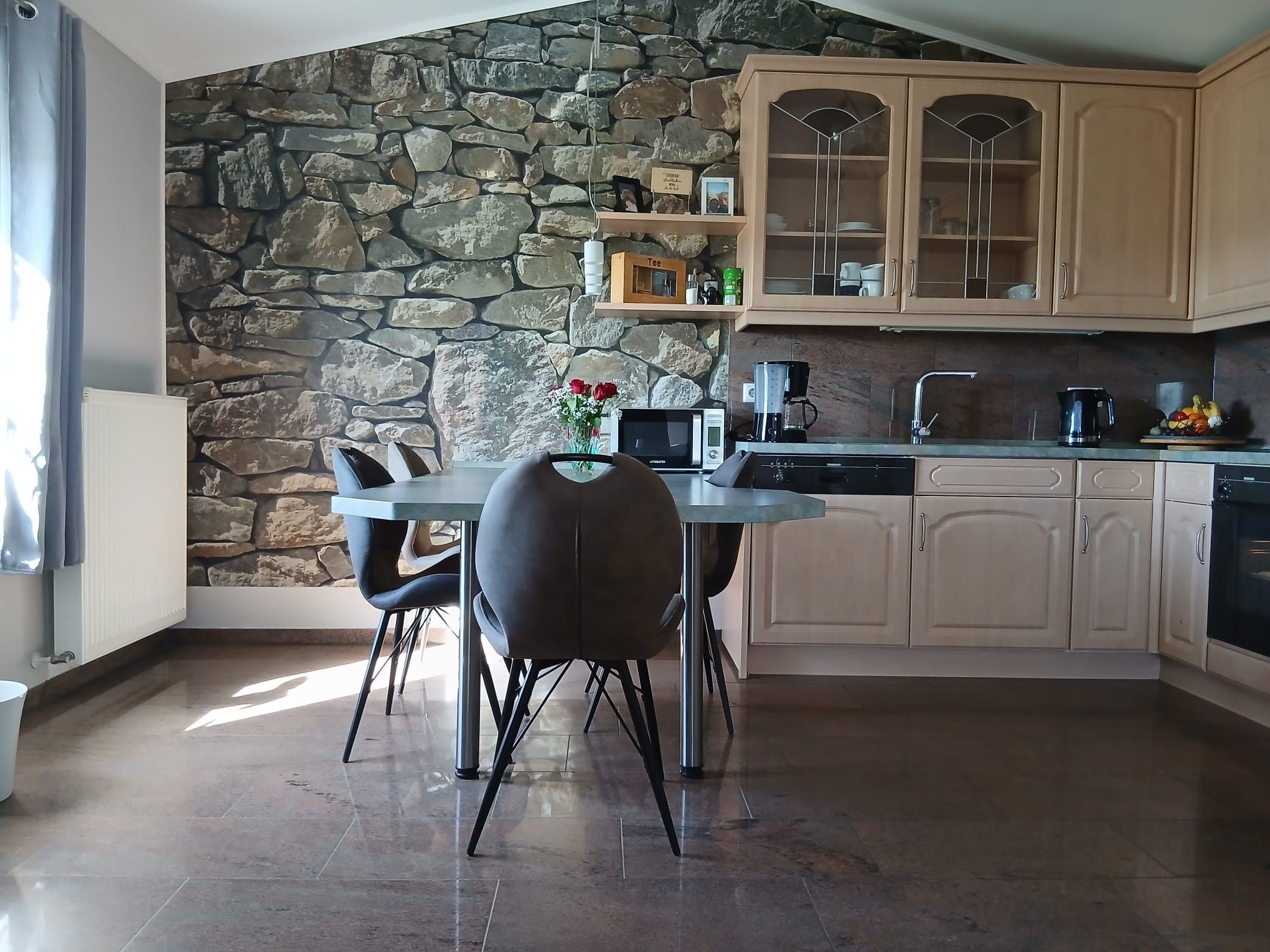A modern kitchen with a stone wall, wooden cabinets, and a dining area with a table and chairs.