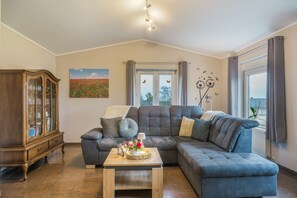 A living room with a sectional sofa, a wooden cabinet, a painting, and a window with curtains.