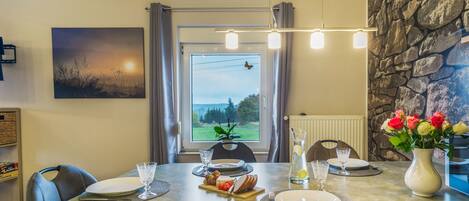 A dining area with a table set for two, a view of the outdoors through a window, and a stone wall.