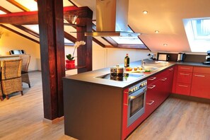 A modern kitchen with a central island, red cabinetry, and a built-in oven. - Holiday apartment Auszeit 3 (Obermaiselstein)