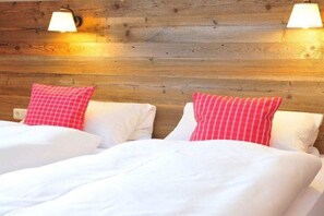A room with two beds, each with white bedding and red pillows. There are wall-mounted lamps on either side of the beds. - Holiday apartment Auszeit 3 (Obermaiselstein)