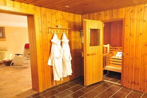 A wooden sauna room with a bench, towels, and a door leading to another area. - Holiday apartment Auszeit 3 (Obermaiselstein)