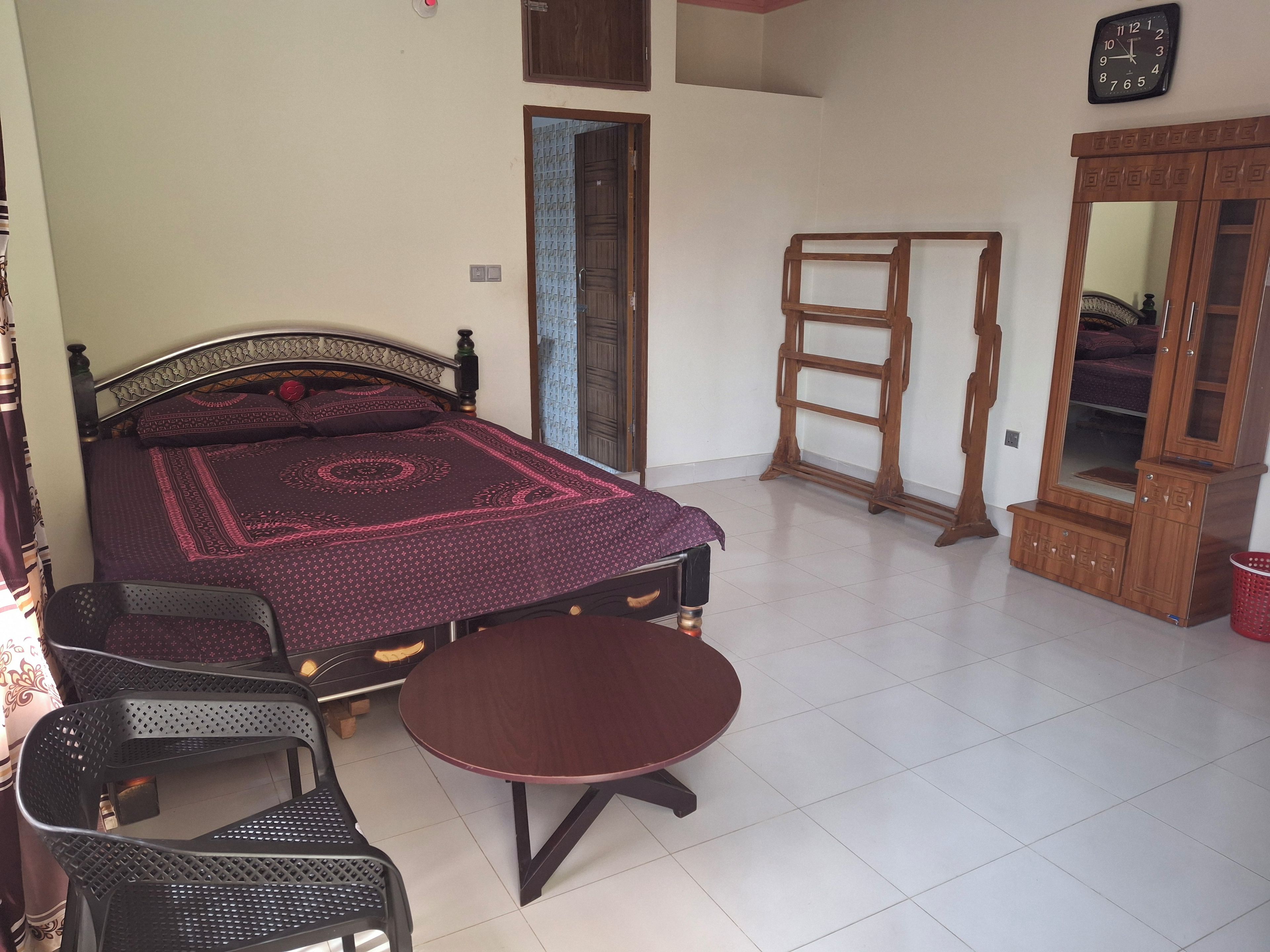 Un dormitorio con cama, armario de madera, mesa redonda, dos sillas y espejo.