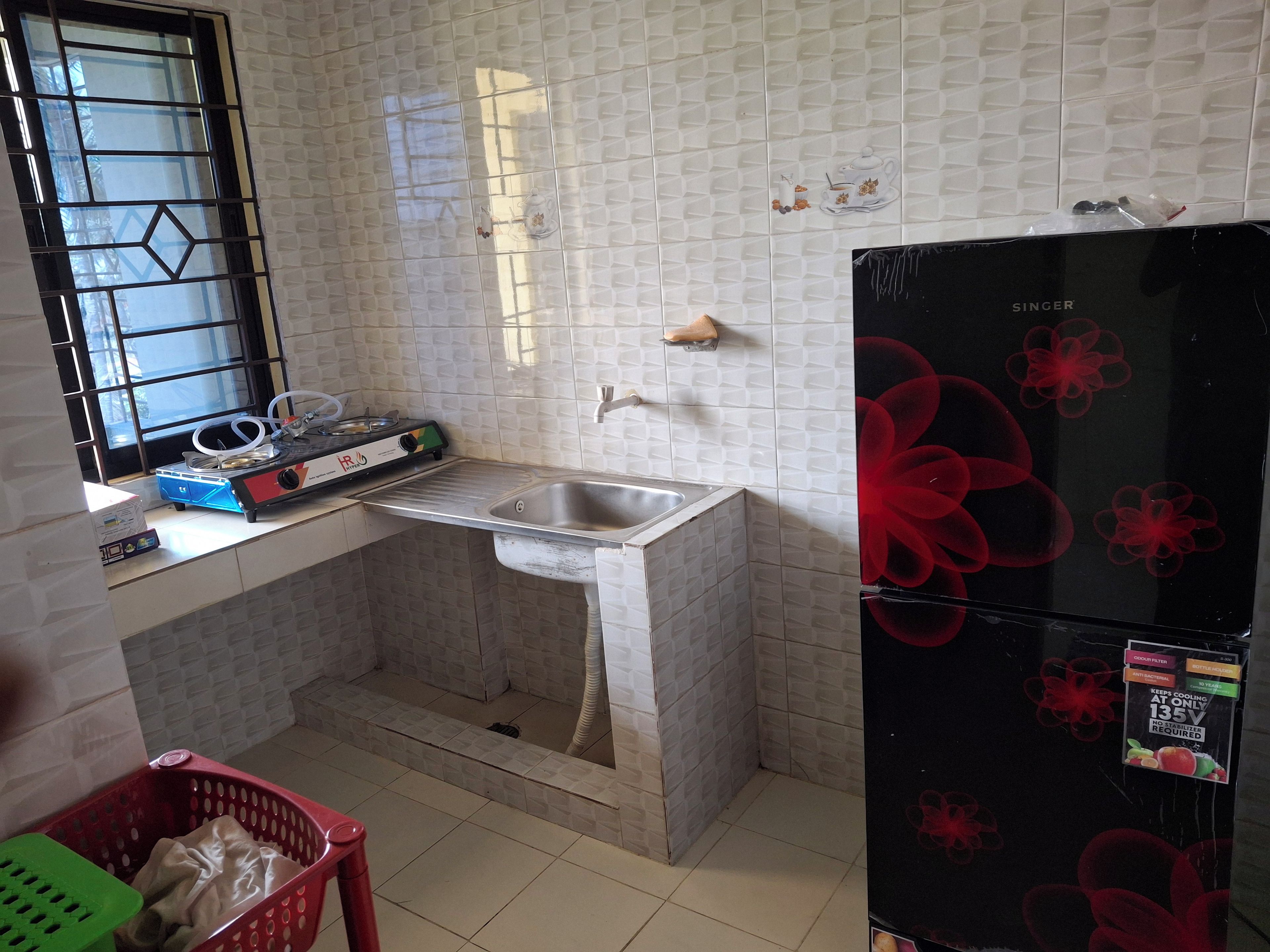 A kitchen with a sink, a window with a metal grid, a refrigerator, and a countertop with various items.