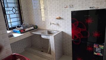 A kitchen with a sink, a window with a metal grid, a refrigerator, and a countertop with various items.