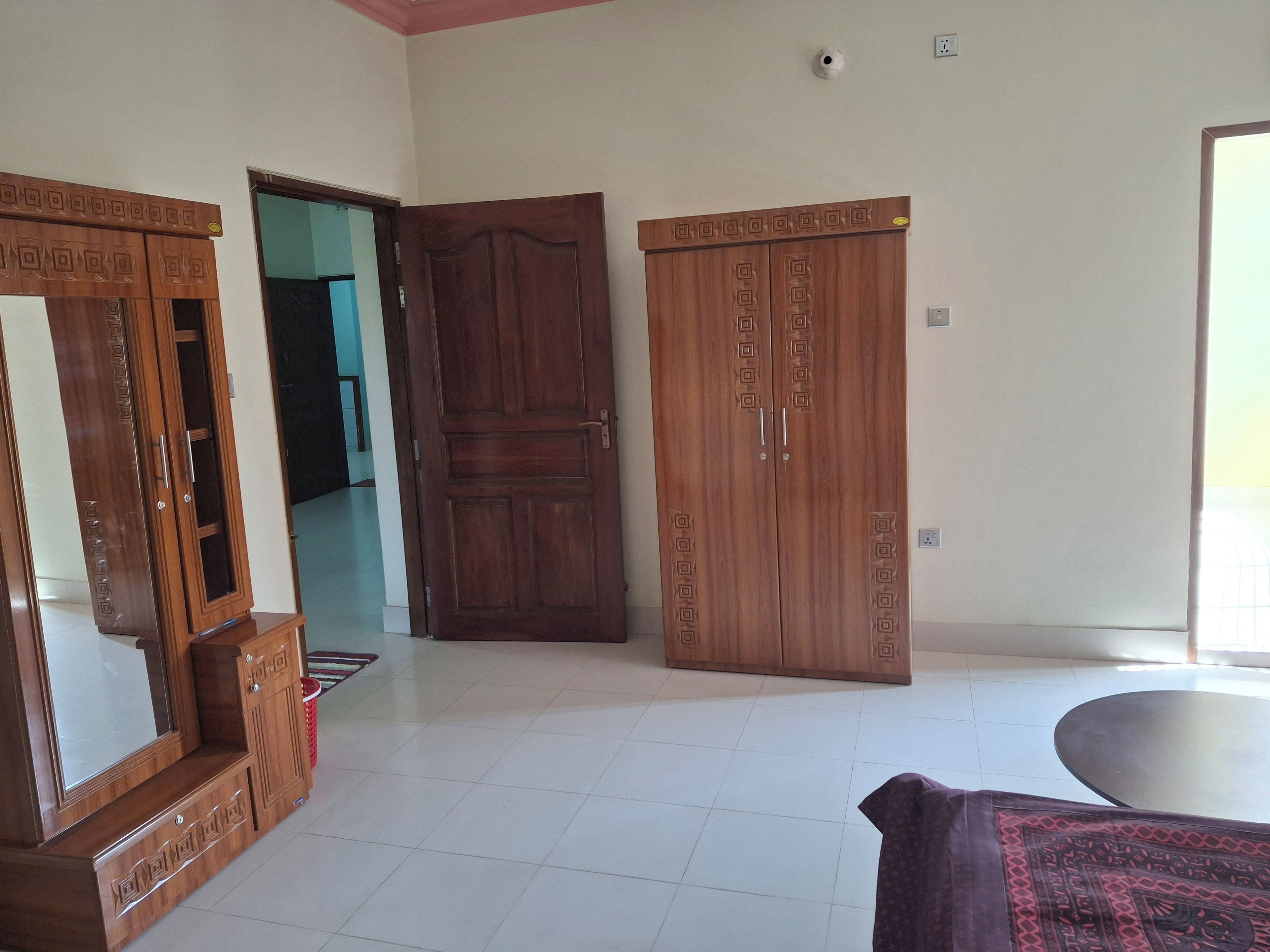 A room with a large wardrobe, a mirror, a patterned rug, and a tiled floor.