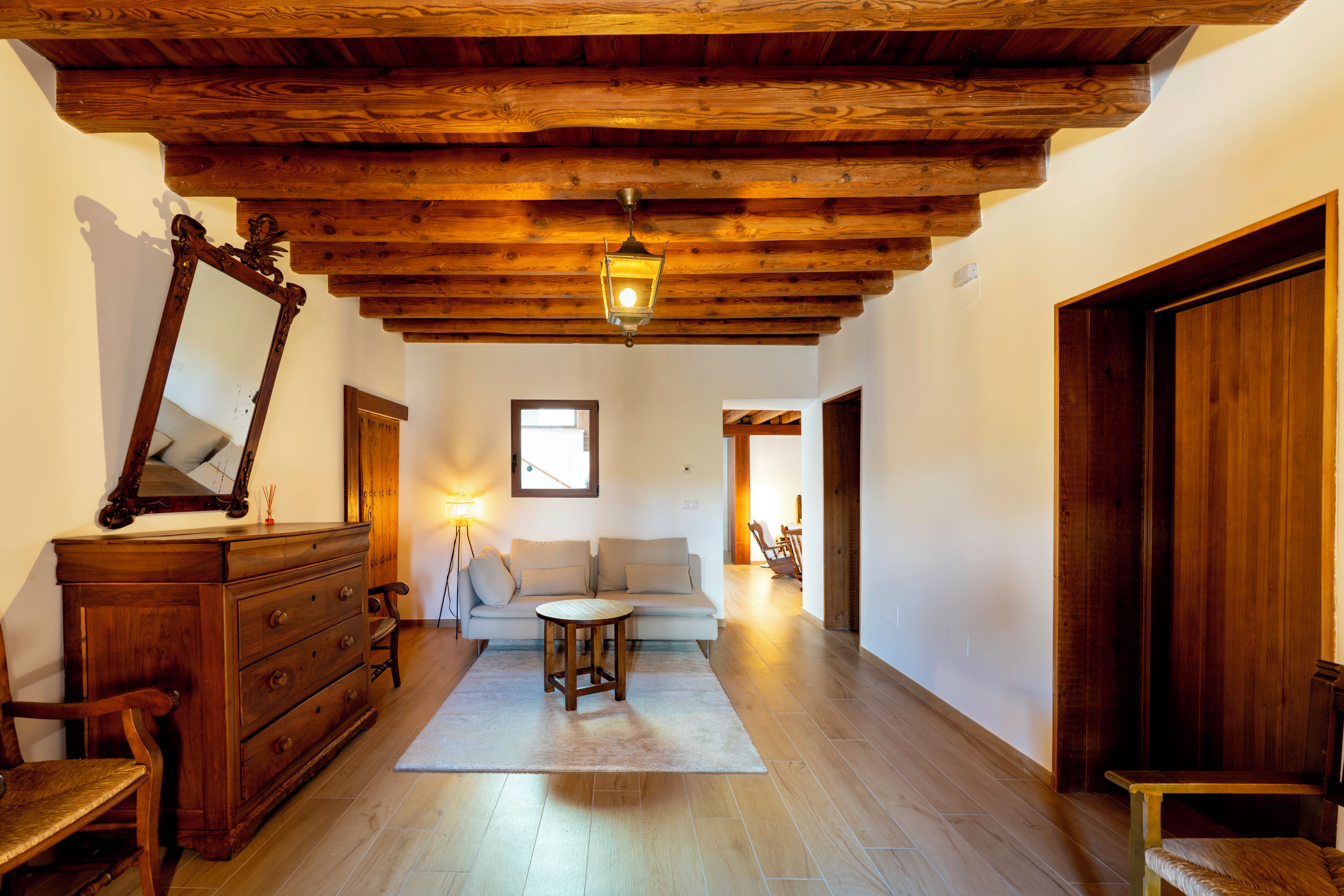 A room with a wooden ceiling, a mirror, a sofa, a table, and a lamp.