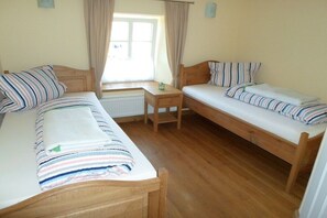 Ein Zimmer mit zwei Holzbett, einem kleinen Tisch und einem Fenster mit Vorhängen.