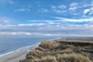 Eine Küstenlandschaft mit Strand, grasbewachsenen Dünen und blauem Himmel.