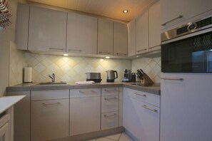 A modern kitchen with stainless steel appliances, a tiled backsplash, and light-colored cabinetry. - Different Living Holiday Apartment 05 Low Tide (Westerland)