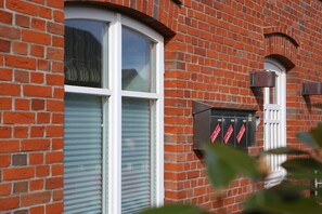A red brick building with a white-framed window and a closed shutter. - Different Living Holiday Apartment 05 Low Tide (Westerland)
