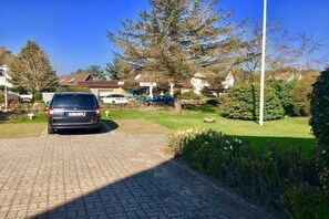 Ein Wohnhof mit parkendem Auto, einem Rasen und Häusern im Hintergrund.