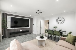 A modern living room with a flat-screen TV, a dining area with a clock, and a staircase. - Stylish 3-Bed | Ebbsfleet & Bluewater | Parking (Northfleet)