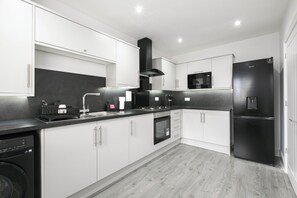 A modern kitchen with white cabinetry, a black stove, and a black refrigerator. - Stylish 3-Bed | Ebbsfleet & Bluewater | Parking (Northfleet)