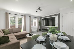 A modern living room with a sofa, dining table set for six, and a flat-screen TV mounted on the wall. - Stylish 3-Bed | Ebbsfleet & Bluewater | Parking (Northfleet)