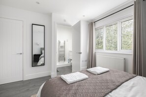 A modern bedroom with a large bed, a mirror, a window with curtains, and a door leading to a bathroom. - Stylish 3-Bed | Ebbsfleet & Bluewater | Parking (Northfleet)