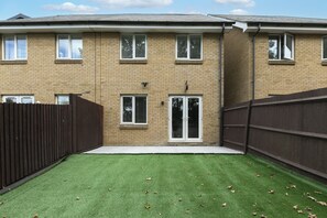 A residential building with a brick facade, multiple windows, and a fenced backyard with artificial grass. - Stylish 3-Bed | Ebbsfleet & Bluewater | Parking (Northfleet)