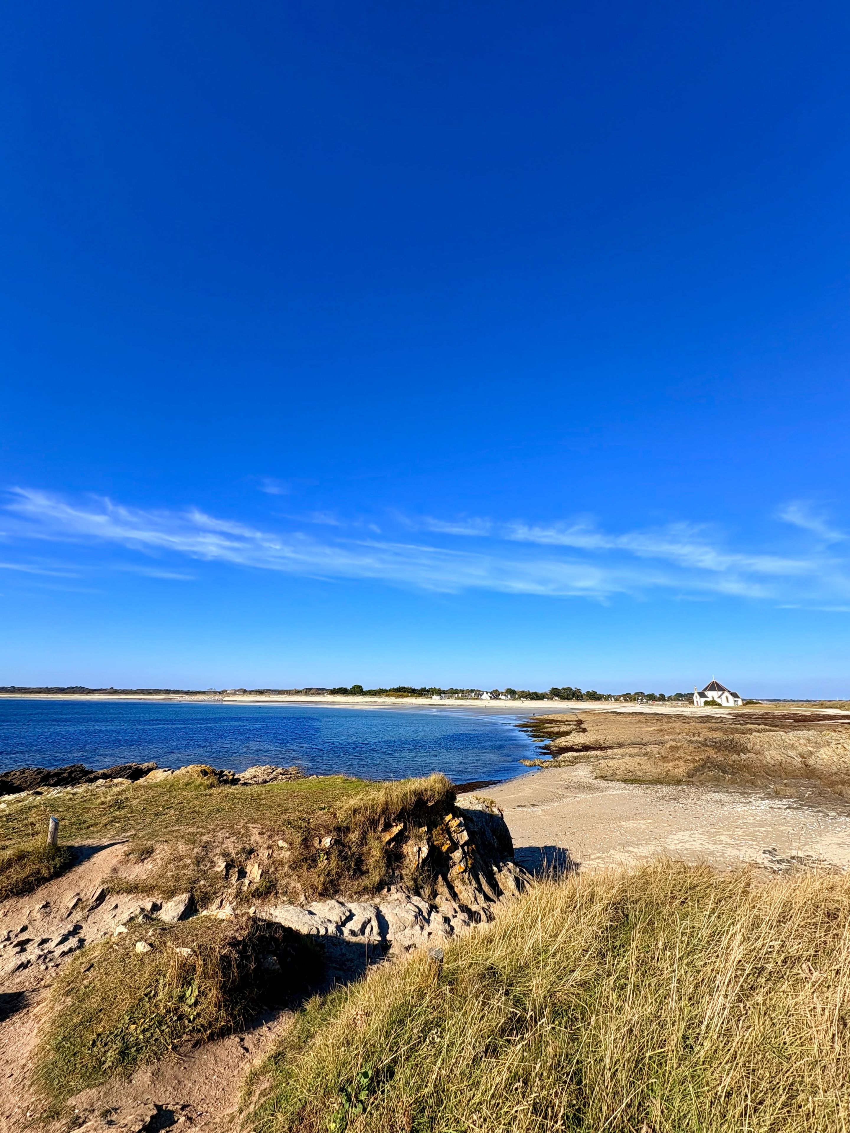 A coastal landscape with a clear sky, a sandy beach, and a white building in the distance.