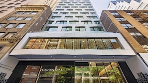 A modern building with a glass facade, a prominent entrance labeled 'The Central 5th Hilton Club,' and a view of the surrounding urban environment.
