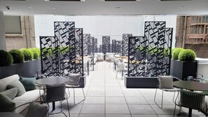Un área de lounge moderna con sofás, mesas y sillas, separada por paneles con un estampado blanco y negro.