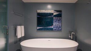 Ein modernes Badezimmer mit freistehender Badewanne, einer Glasdusche und einem großen abstrakten Gemälde an der Wand.