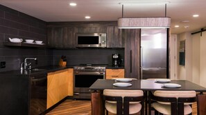A modern kitchen with dark cabinetry, stainless steel appliances, and a wooden island with seating. - Big Island Ocean Tower Stay with Partial Ocean View, Pools & Waikoloa Resort Fun (Waikoloa Village)