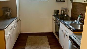 A kitchen with wooden flooring, white cabinets, a built-in oven, a dishwasher, and a window with a plant.