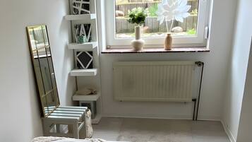 A bedroom with a large bed, a window with a view of greenery, a radiator, and a white shelving unit.