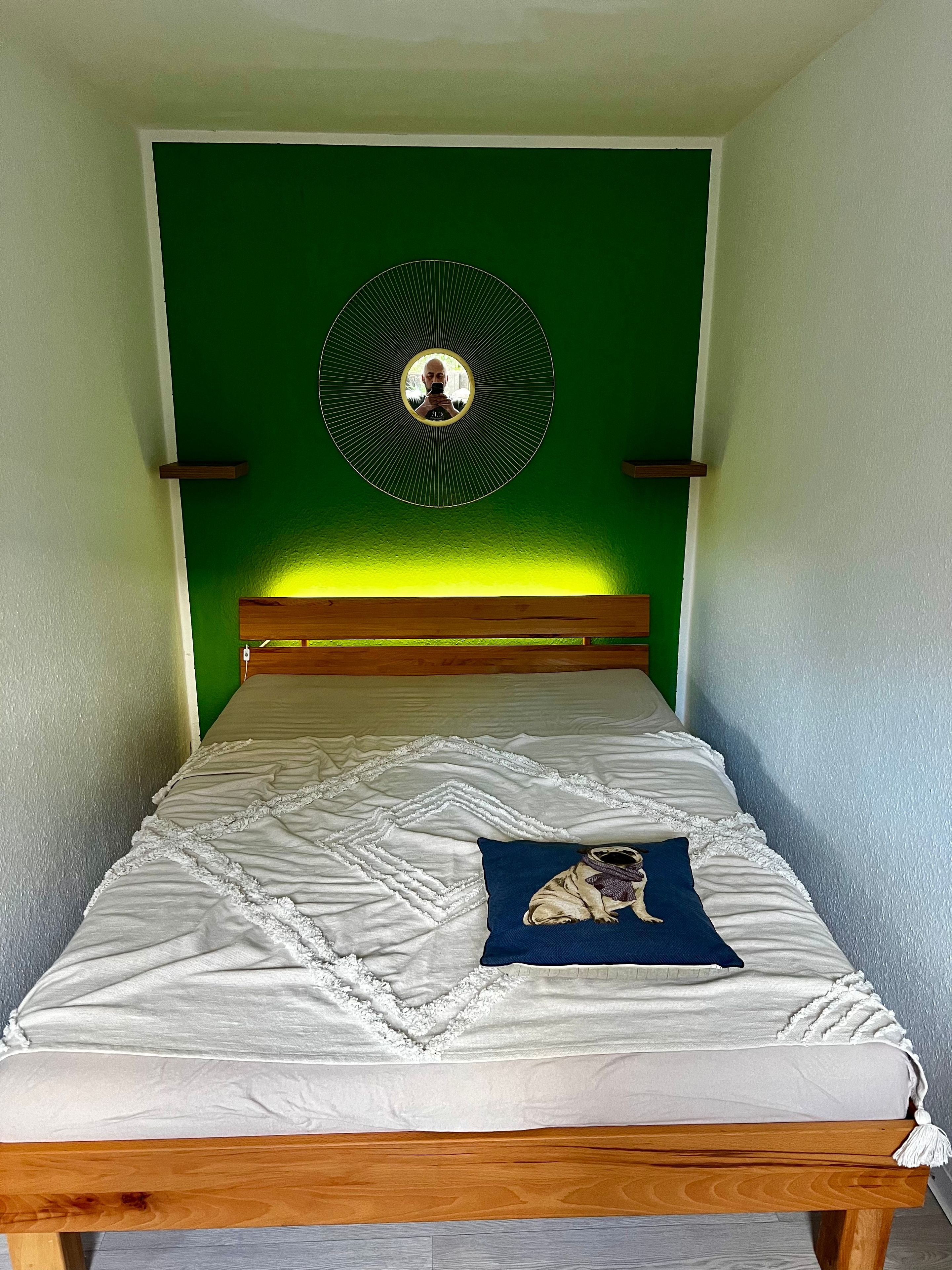 A bed with a white quilt, a blue pillow with a dog image, and a circular wall decoration.