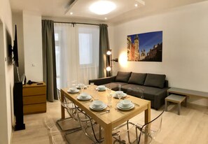A dining area with a wooden table set for four, a sofa, and a painting of a cityscape on the wall. - Spacious 1-bedroom apartment in Prague Old Town (Prague)